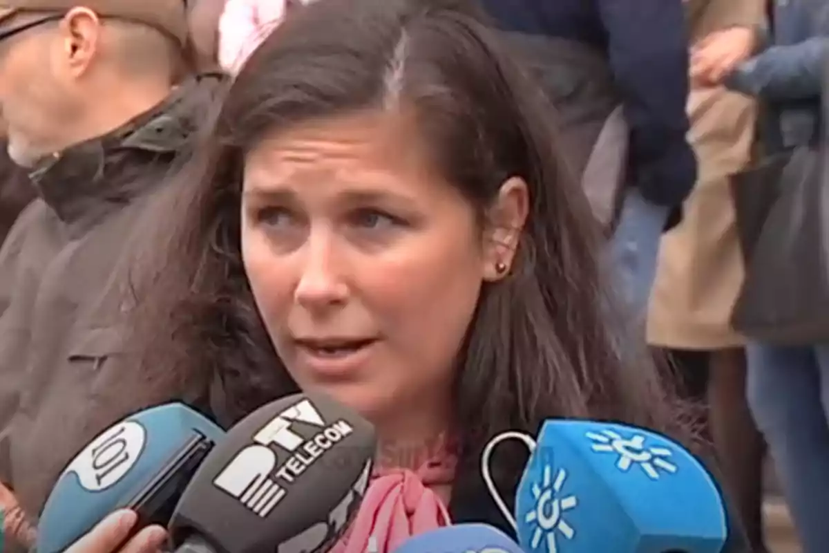 Mujer de cabello oscuro hablando frente a varios micrófonos de diferentes medios de comunicación en un evento al aire libre Mujer de cabello oscuro hablando frente a varios micrófonos de diferentes medios de comunicación en un evento al aire libre