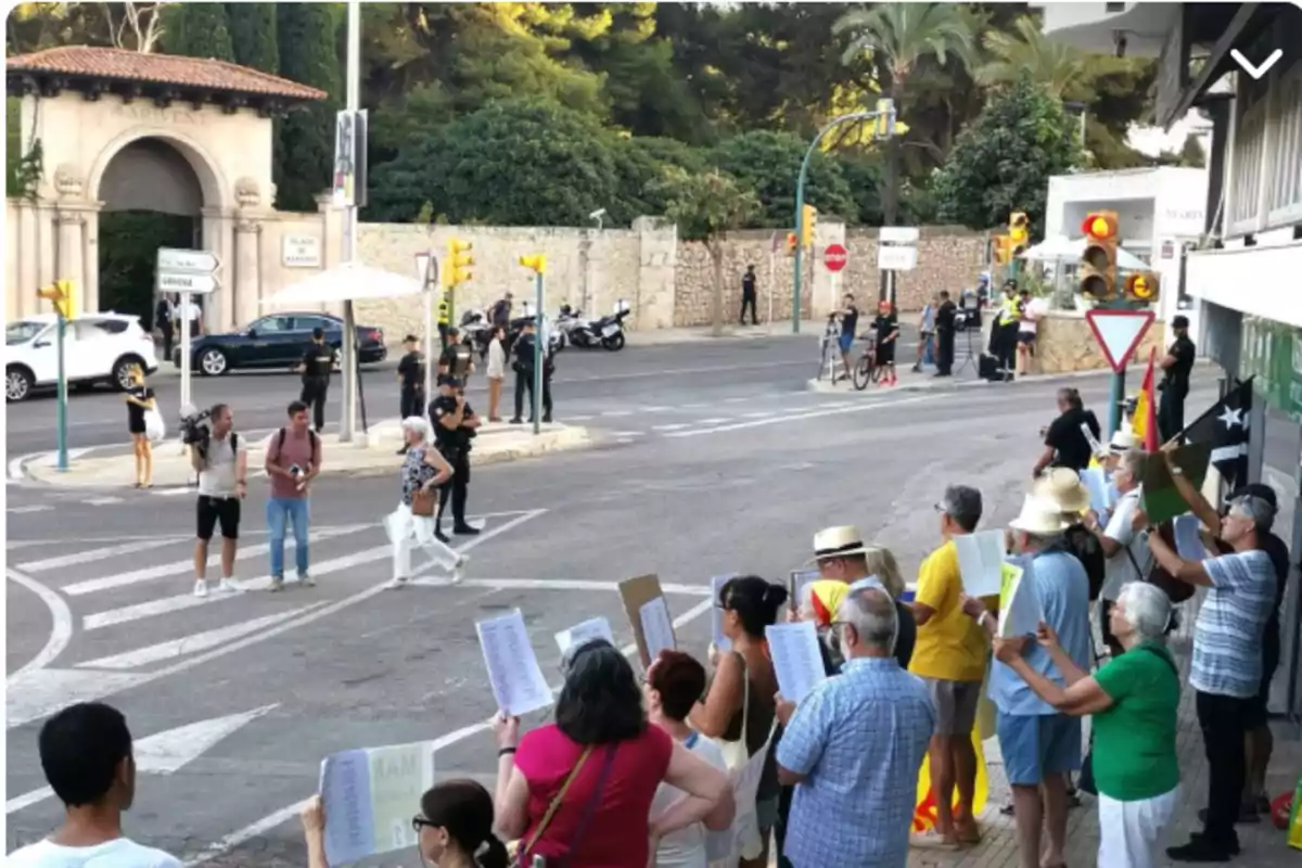 Un grupo de personas sostiene pancartas en una esquina mientras varios policías vigilan la zona y algunos periodistas cubren el evento en una calle con tráfico detenido Un grupo de personas sostiene pancartas en una esquina mientras varios policías vigilan la zona y algunos periodistas cubren el evento en una calle con tráfico detenido