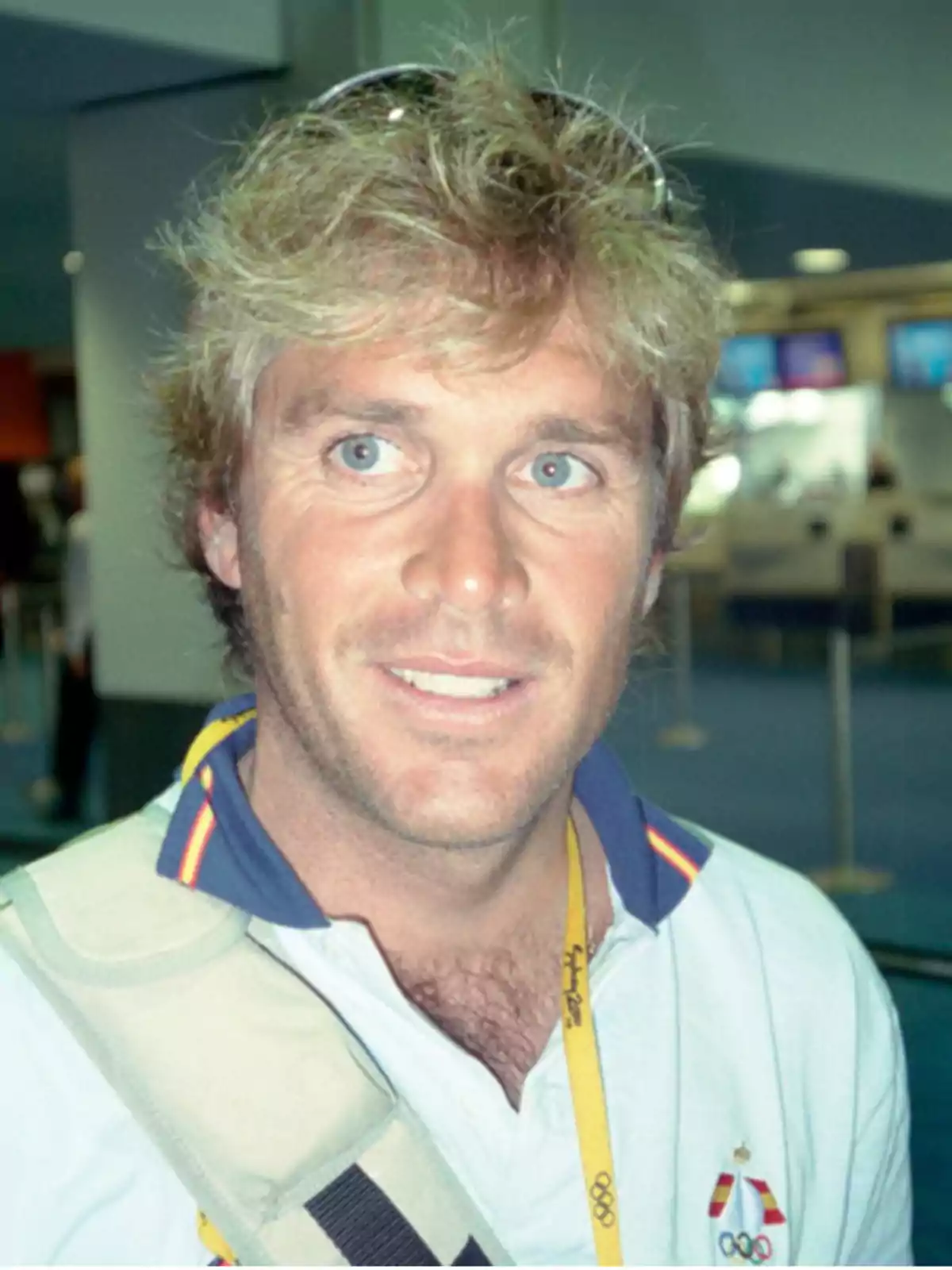 Blond man with light eyes wearing a white t-jersey and sunglasses on his head in an indoor setting