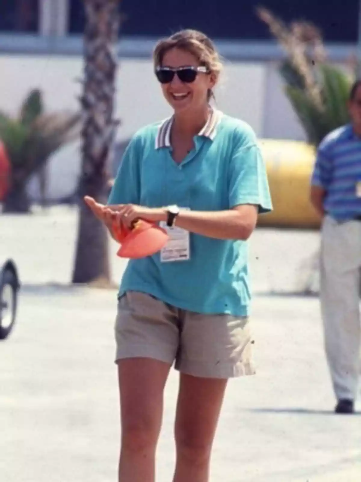 Smiling woman with sunglasses and a blue t-jersey holding an orange cone in an outdoor setting