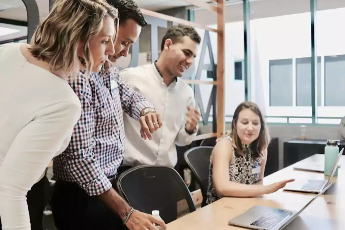 Cuatro personas colaboran en una oficina mientras observan la pantalla de una laptop sobre una mesa