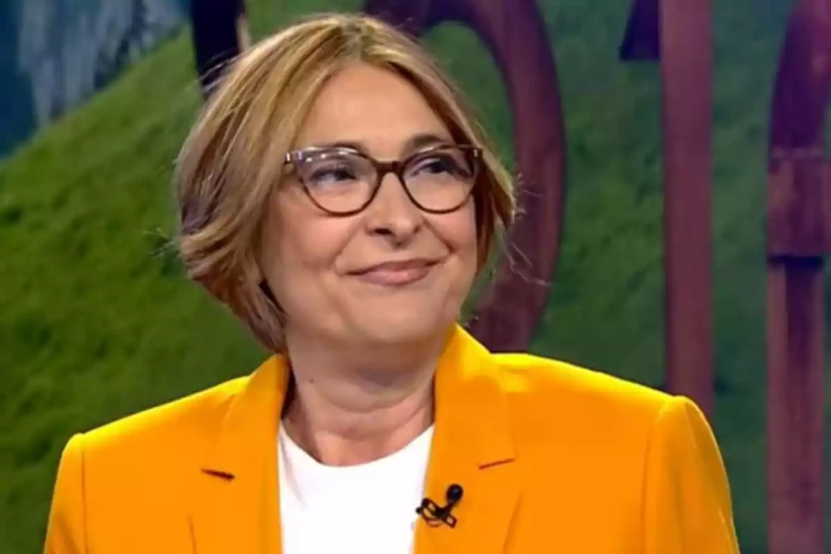 Mujer de cabello corto y gafas con saco amarillo sonriendo en un estudio de televisión Mujer de cabello corto y gafas con saco amarillo sonriendo en un estudio de televisión