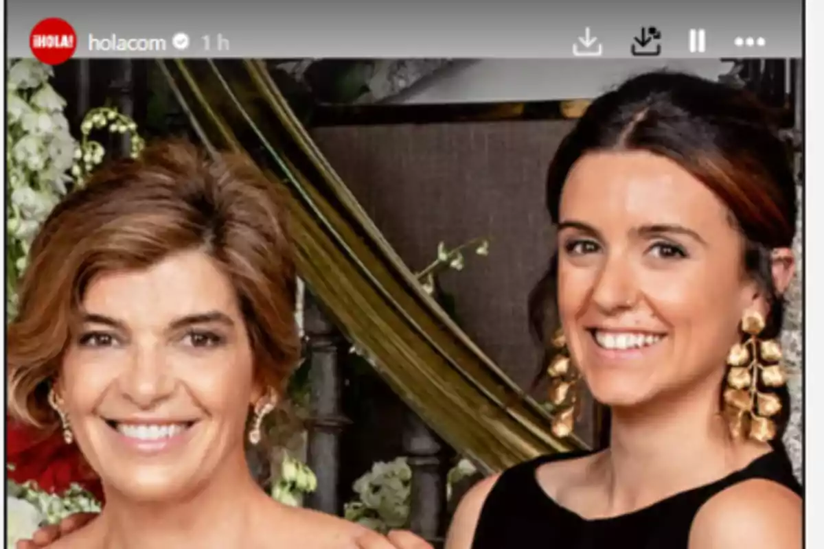 Dos mujeres sonríen frente a la cámara, una lleva un vestido negro y grandes pendientes dorados, la otra tiene el cabello corto y luce un peinado elegante, ambas posan en un ambiente decorado con flores. Dos mujeres sonríen frente a la cámara, una lleva un vestido negro y grandes pendientes dorados, la otra tiene el cabello corto y luce un peinado elegante, ambas posan en un ambiente decorado con flores.