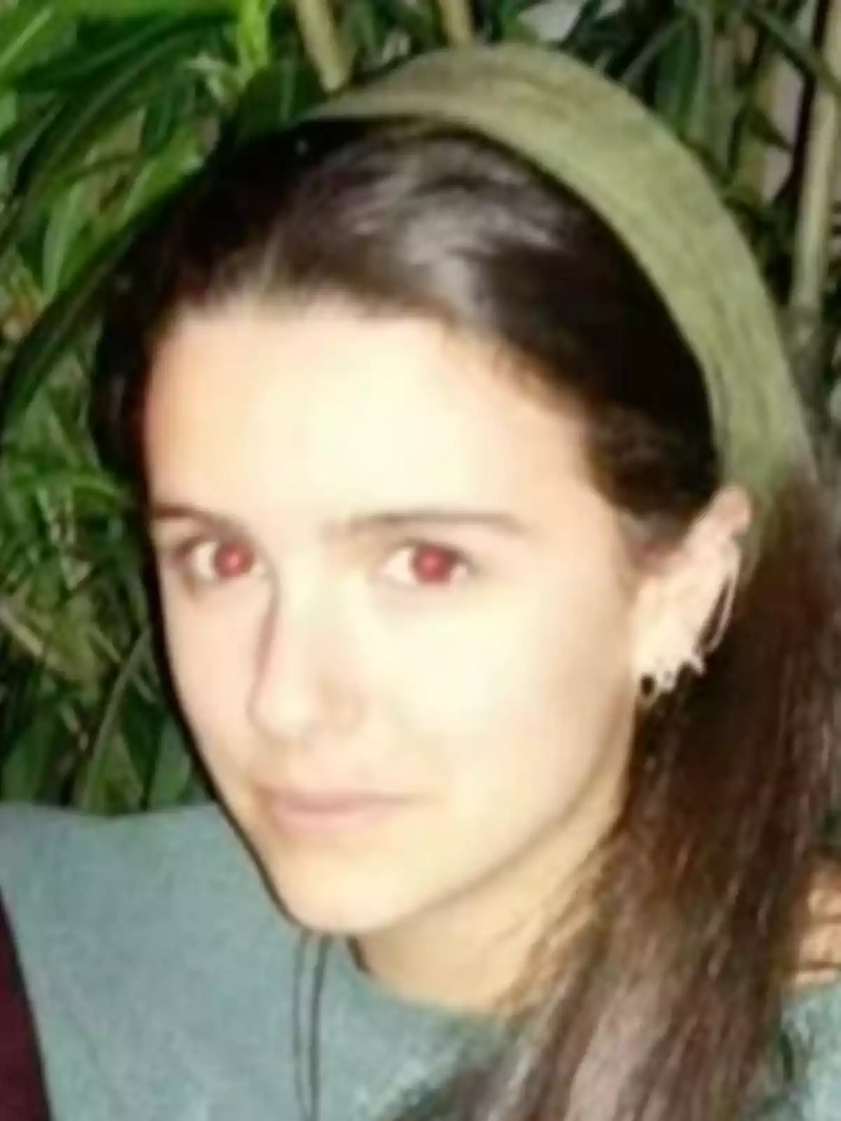 Joven de cabello largo y oscuro con diadema verde, fondo de plantas y mirada directa a la cámara Joven de cabello largo y oscuro con diadema verde, fondo de plantas y mirada directa a la cámara
