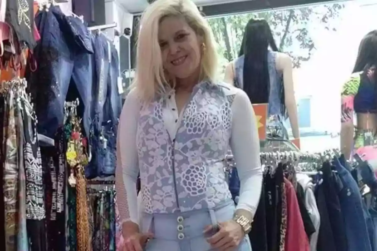 Mujer rubia posando y sonriendo en una tienda de ropa rodeada de prendas colgadas y maniquíes al fondo Mujer rubia posando y sonriendo en una tienda de ropa rodeada de prendas colgadas y maniquíes al fondo