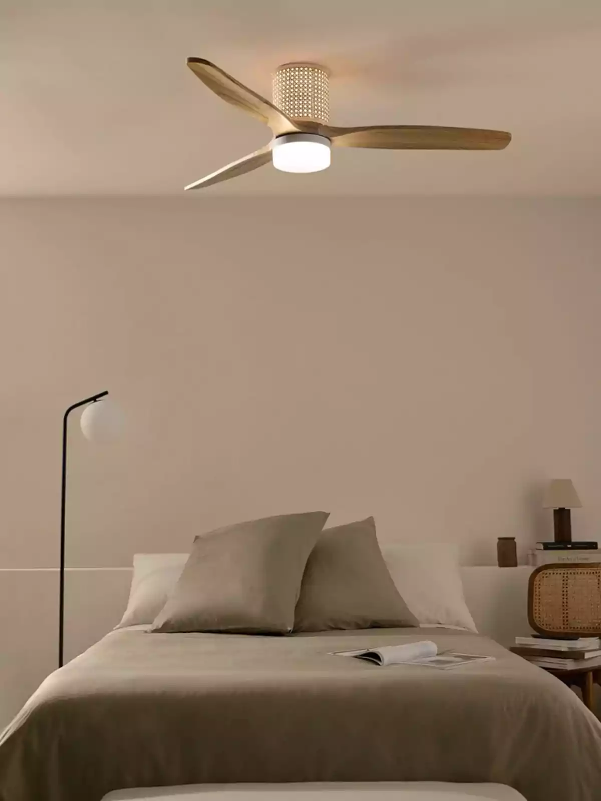 Dormitorio moderno con cama de sábanas beige, ventilador de techo de madera, lámpara de pie y mesa de noche con libros y lámpara pequeña Dormitorio moderno con cama de sábanas beige, ventilador de techo de madera, lámpara de pie y mesa de noche con libros y lámpara pequeña
