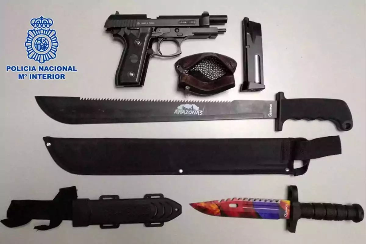 Armas incautadas por la policía nacional incluyendo una pistola, un cargador, municiones, un machete y un cuchillo con funda sobre una mesa Armas incautadas por la policía nacional incluyendo una pistola, un cargador, municiones, un machete y un cuchillo con funda sobre una mesa