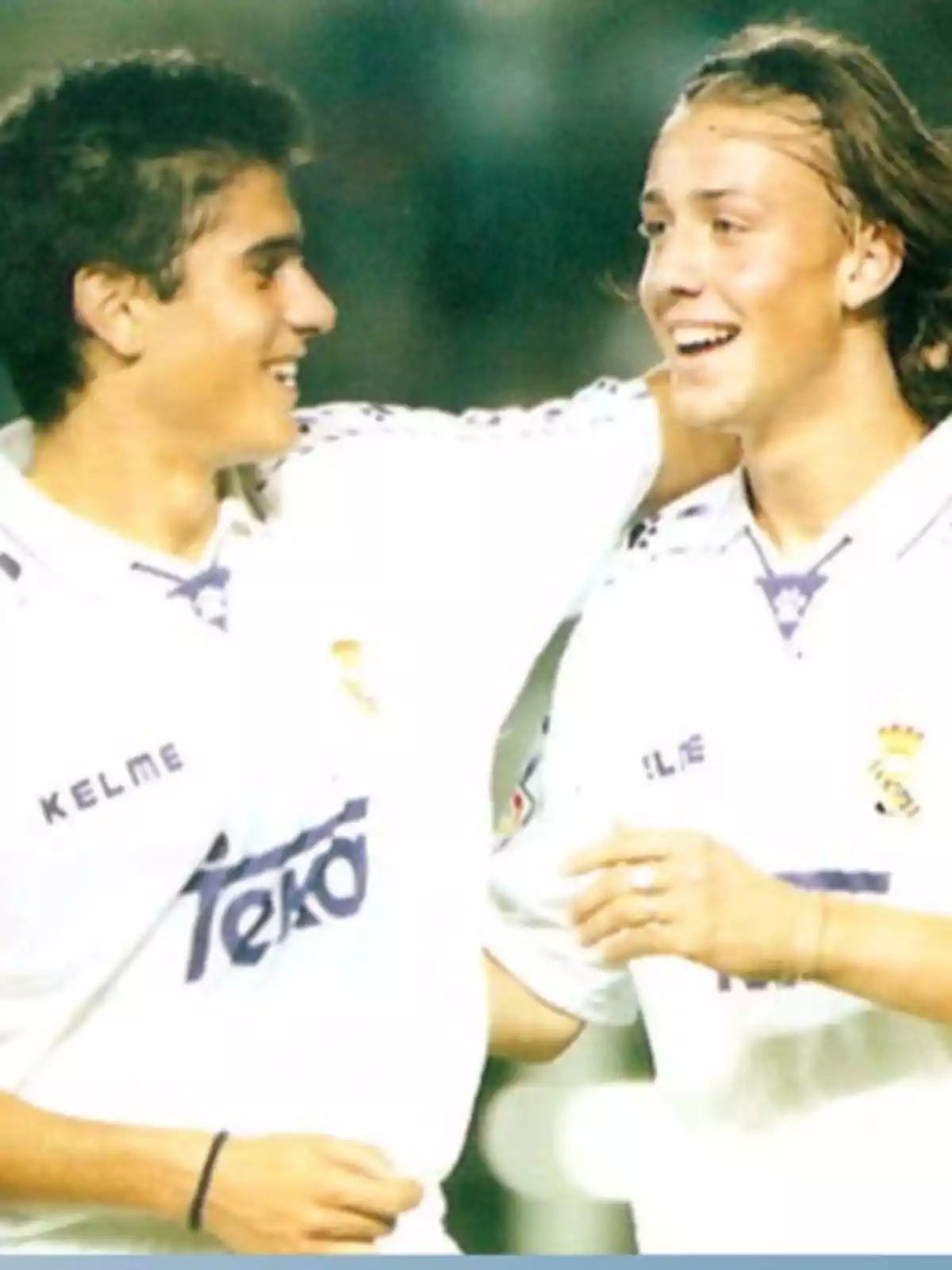 Dos jóvenes futbolistas con uniforme blanco del Real Madrid sonríen y se abrazan en el campo de juego Dos jóvenes futbolistas con uniforme blanco del Real Madrid sonríen y se abrazan en el campo de juego