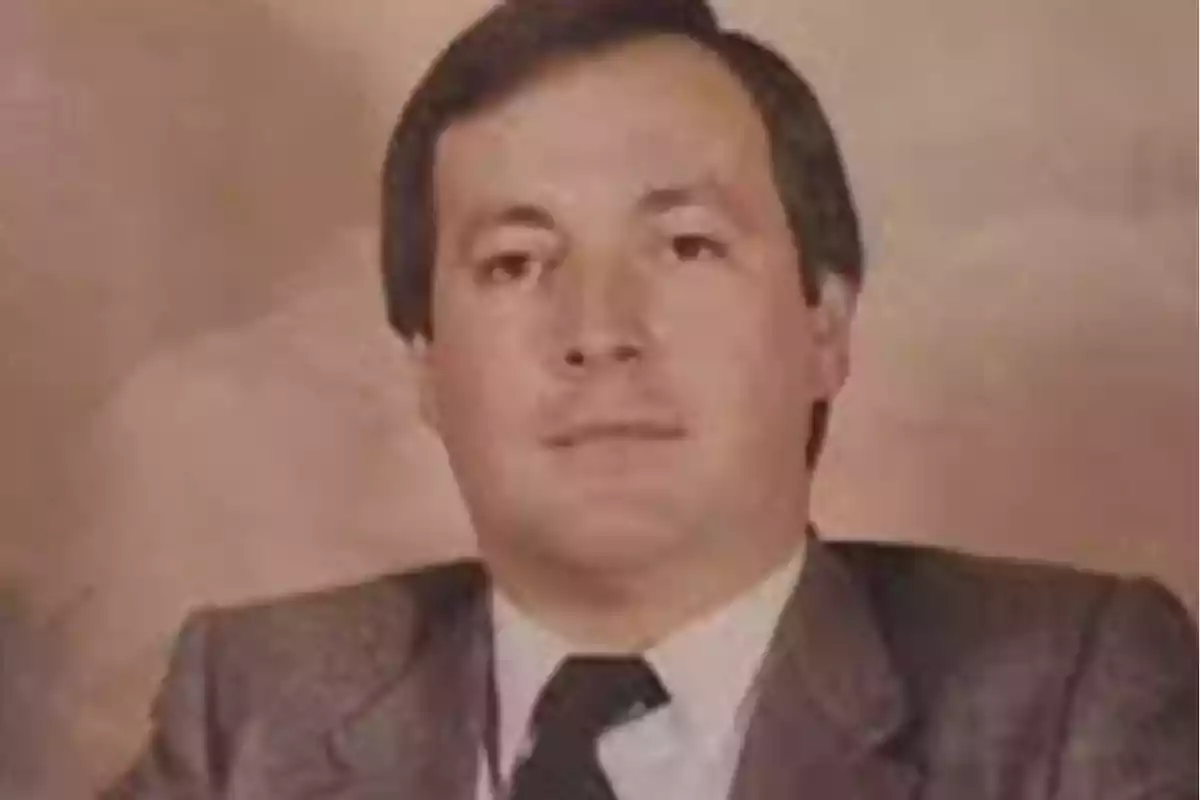 Hombre de cabello corto y oscuro vistiendo traje formal con corbata frente a un fondo beige Hombre de cabello corto y oscuro vistiendo traje formal con corbata frente a un fondo beige