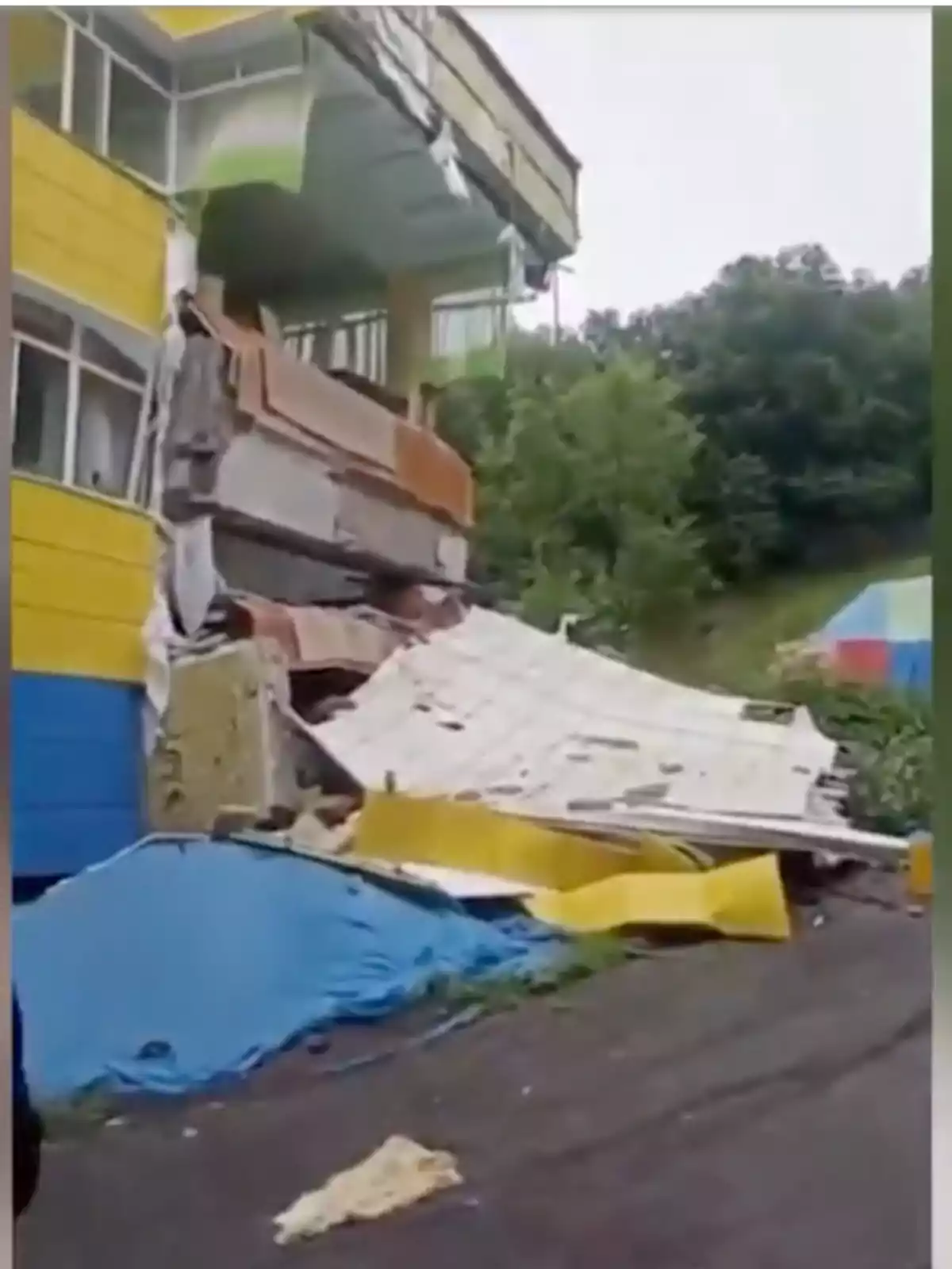 Edificio amarillo con parte de su estructura colapsada y escombros en el suelo frente a una zona arbolada Edificio amarillo con parte de su estructura colapsada y escombros en el suelo frente a una zona arbolada