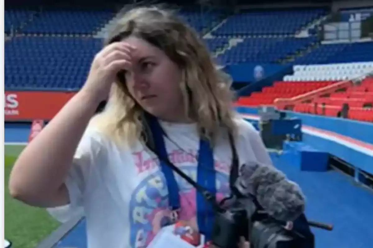Mujer con camiseta blanca y cámara en la mano dentro de un estadio vacío con asientos rojos y azules Mujer con camiseta blanca y cámara en la mano dentro de un estadio vacío con asientos rojos y azules
