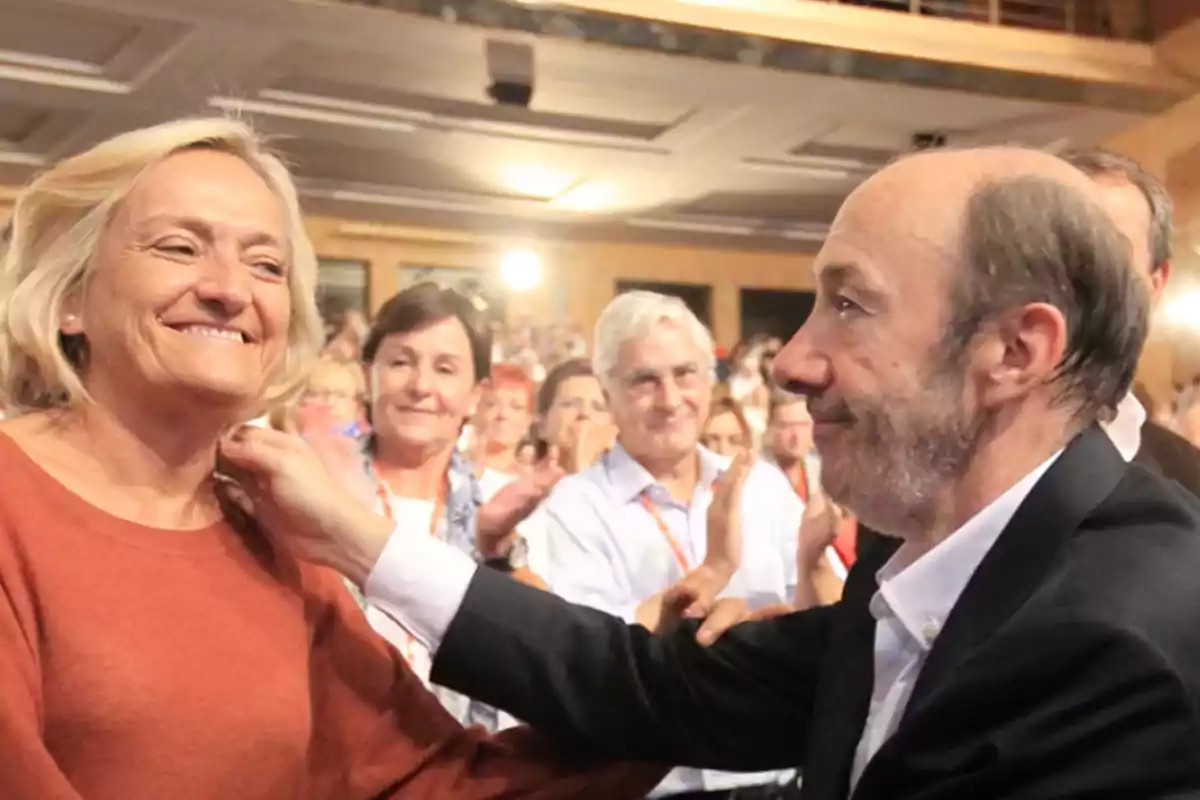Un hombre sonriente coloca una medalla a una mujer en un evento con público aplaudiendo al fondo Un hombre sonriente coloca una medalla a una mujer en un evento con público aplaudiendo al fondo