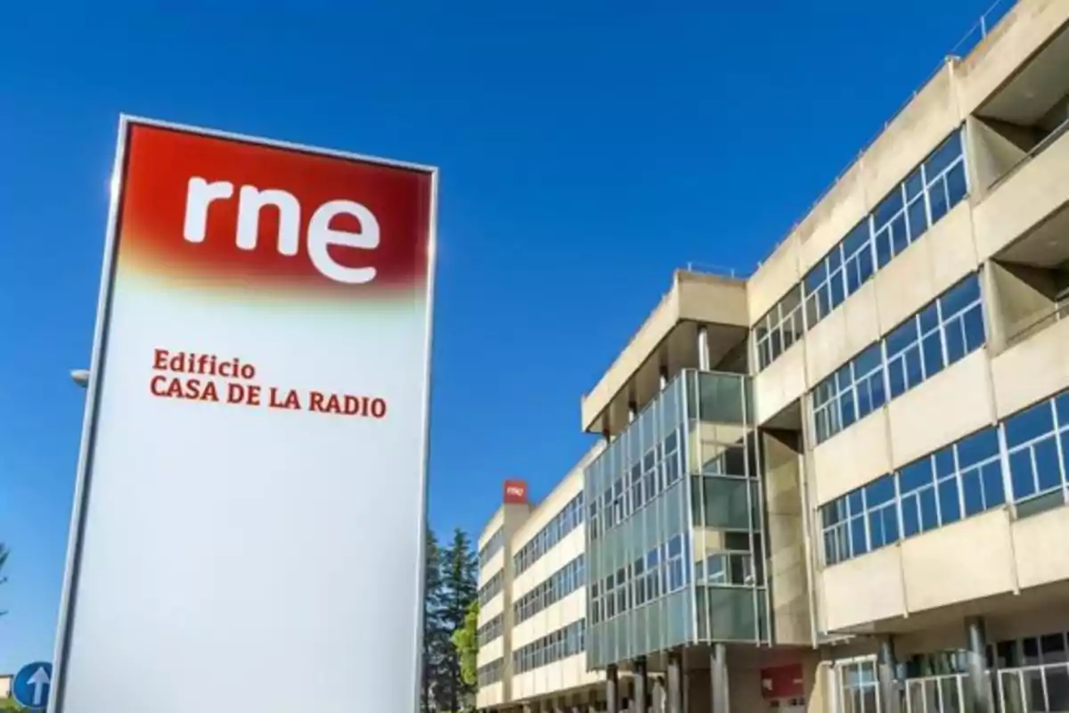 Edificio moderno de varios pisos con muchas ventanas y un letrero grande de rne que indica Edificio Casa de la Radio bajo un cielo azul despejado Edificio moderno de varios pisos con muchas ventanas y un letrero grande de rne que indica Edificio Casa de la Radio bajo un cielo azul despejado