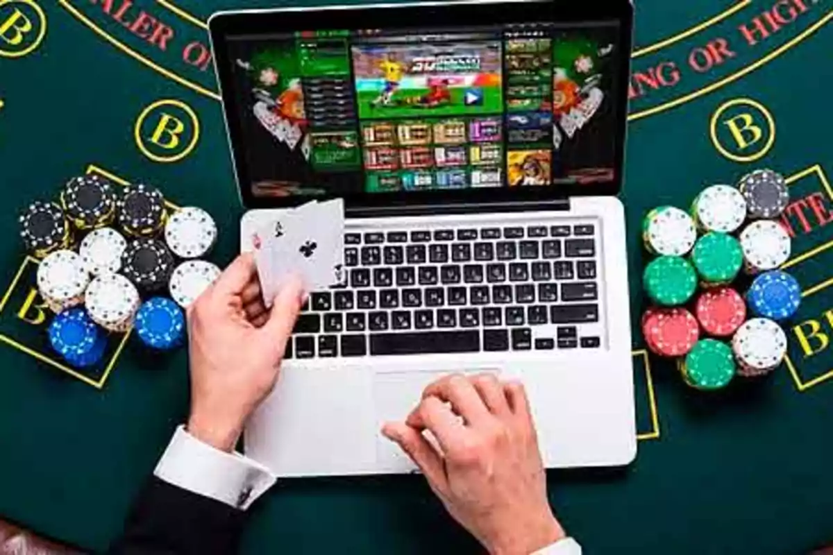 Persona jugando póker en línea en una computadora portátil con fichas de casino y cartas sobre una mesa verde