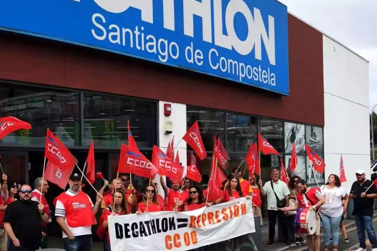 Personas manifestándose frente a una tienda de Decathlon en Santiago de Compostela con banderas rojas de CCOO y una pancarta que denuncia represión Personas manifestándose frente a una tienda de Decathlon en Santiago de Compostela con banderas rojas de CCOO y una pancarta que denuncia represión