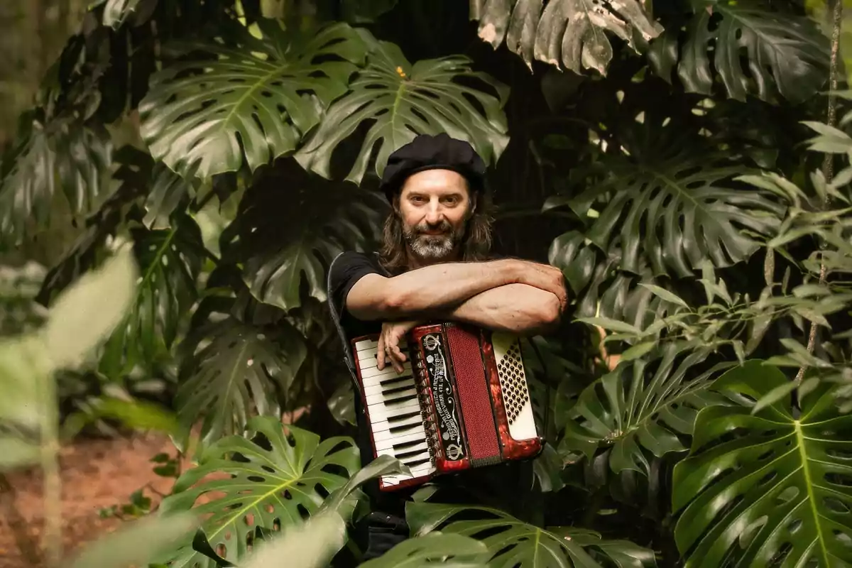 Hombre con boina y barba abrazando un acordeón rojo entre hojas grandes de monstera en un entorno selvático Hombre con boina y barba abrazando un acordeón rojo entre hojas grandes de monstera en un entorno selvático