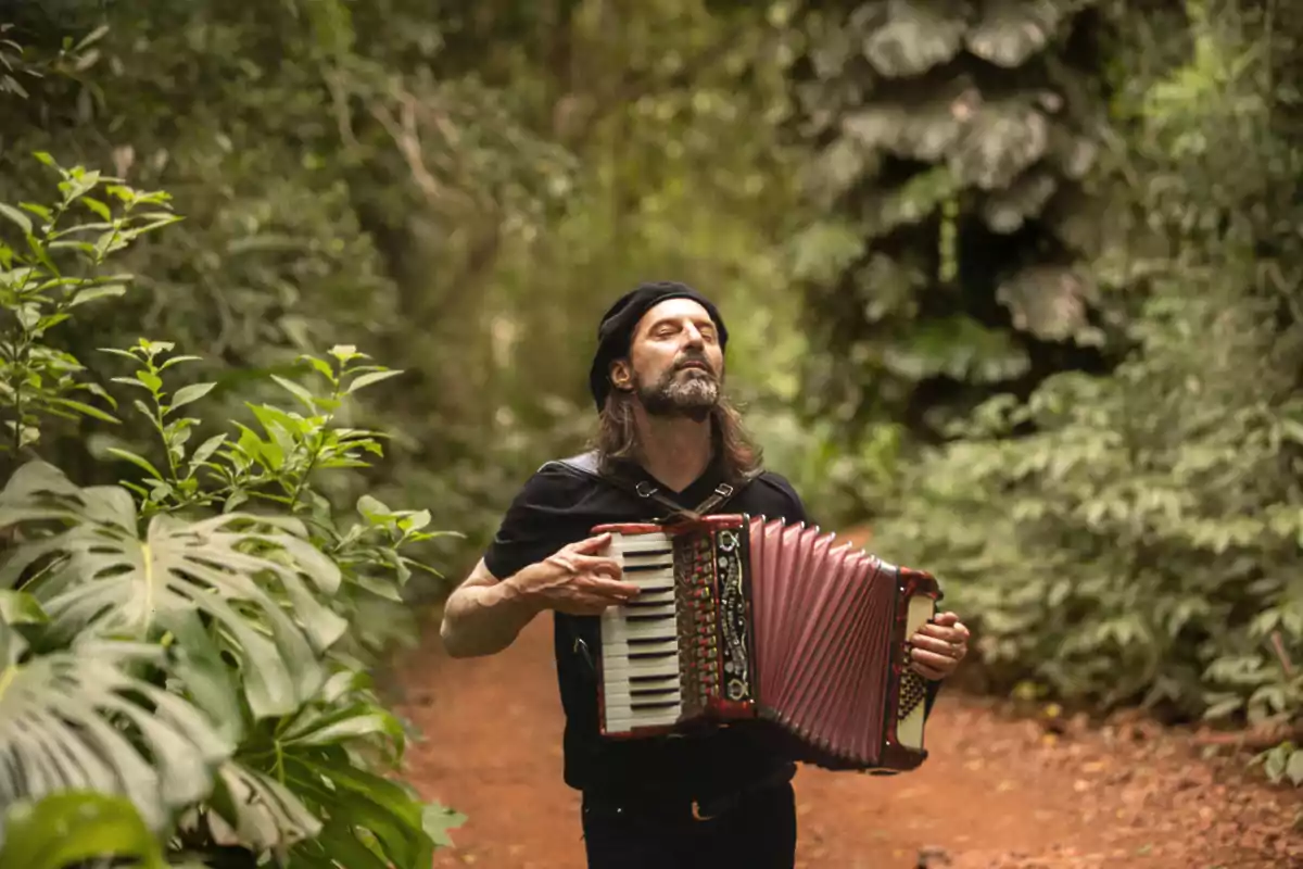 Hombre con boina tocando un acordeón en un sendero rodeado de vegetación exuberante