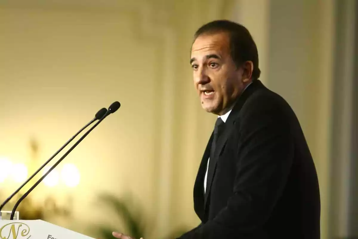 Hombre de traje oscuro hablando en un podio con dos micrófonos en un ambiente formal
