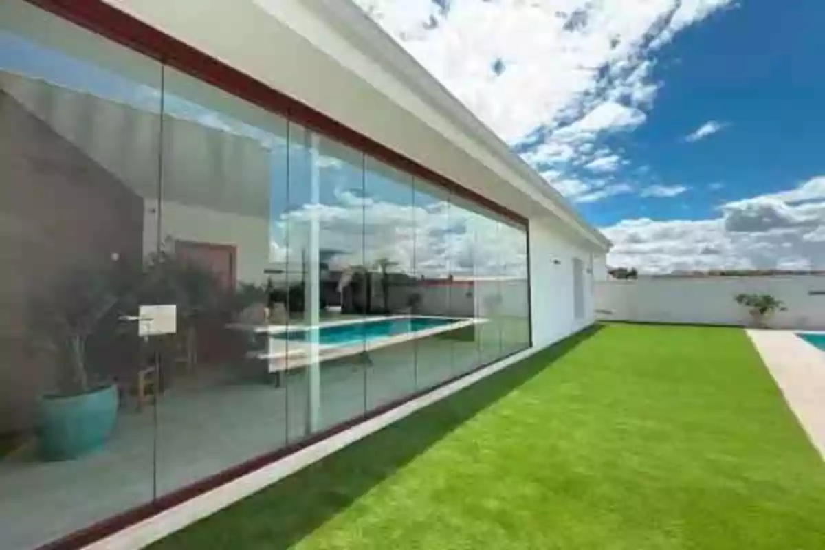 Casa moderna con ventanales de cristal, césped verde y piscina bajo un cielo azul con nubes Casa moderna con ventanales de cristal, césped verde y piscina bajo un cielo azul con nubes