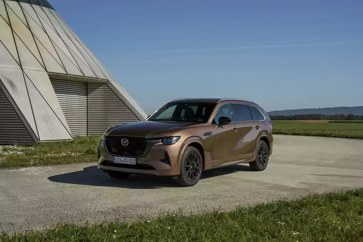SUV Mazda color cobre estacionada sobre un camino de concreto junto a una estructura moderna de metal en un entorno campestre bajo un cielo despejado SUV Mazda color cobre estacionada sobre un camino de concreto junto a una estructura moderna de metal en un entorno campestre bajo un cielo despejado