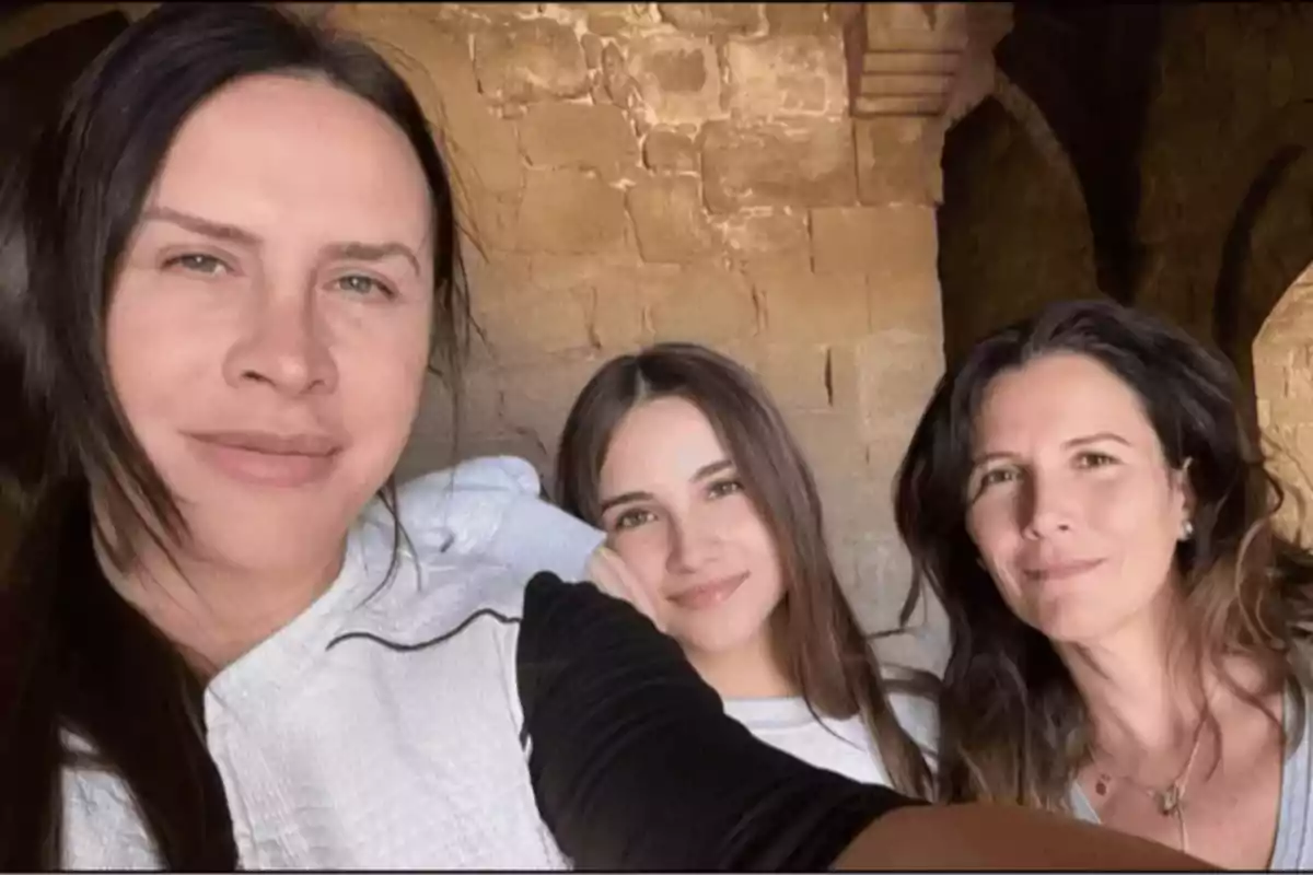 Tres mujeres sonríen mientras posan para una selfie frente a una pared de piedra antigua Tres mujeres sonríen mientras posan para una selfie frente a una pared de piedra antigua