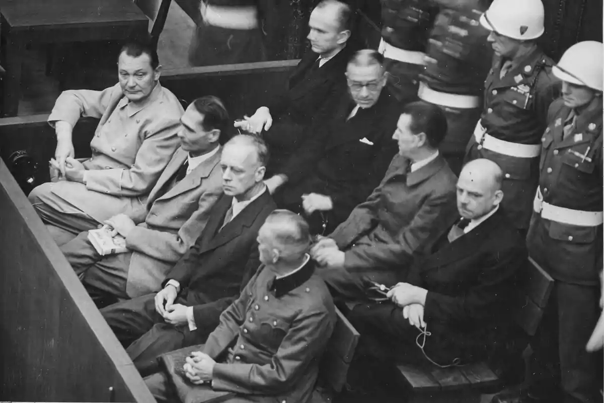 Varios hombres sentados en un tribunal con soldados uniformados de pie detrás de ellos Varios hombres sentados en un tribunal con soldados uniformados de pie detrás de ellos