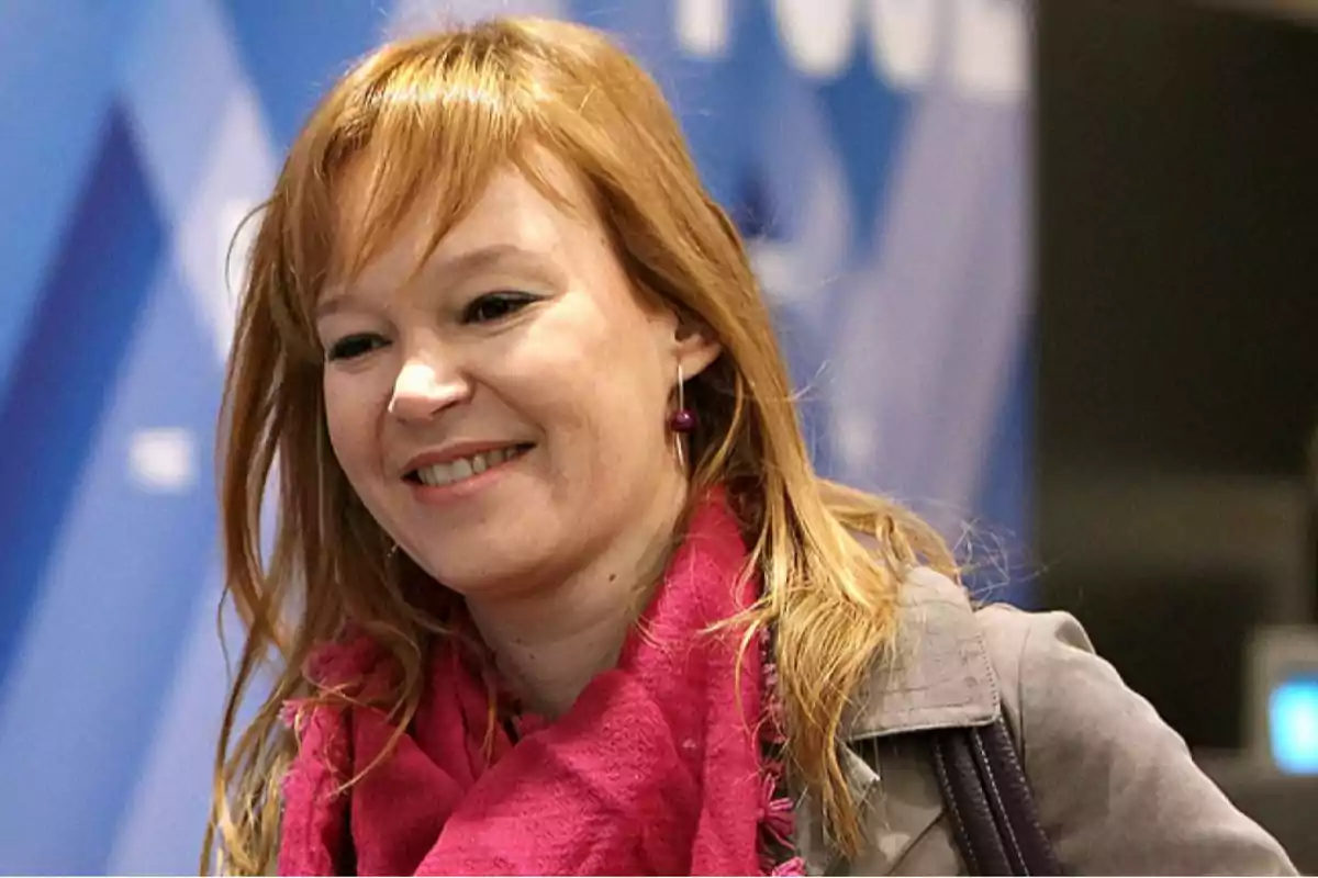 Mujer pelirroja sonriendo con bufanda rosa y fondo azul desenfocado Mujer pelirroja sonriendo con bufanda rosa y fondo azul desenfocado