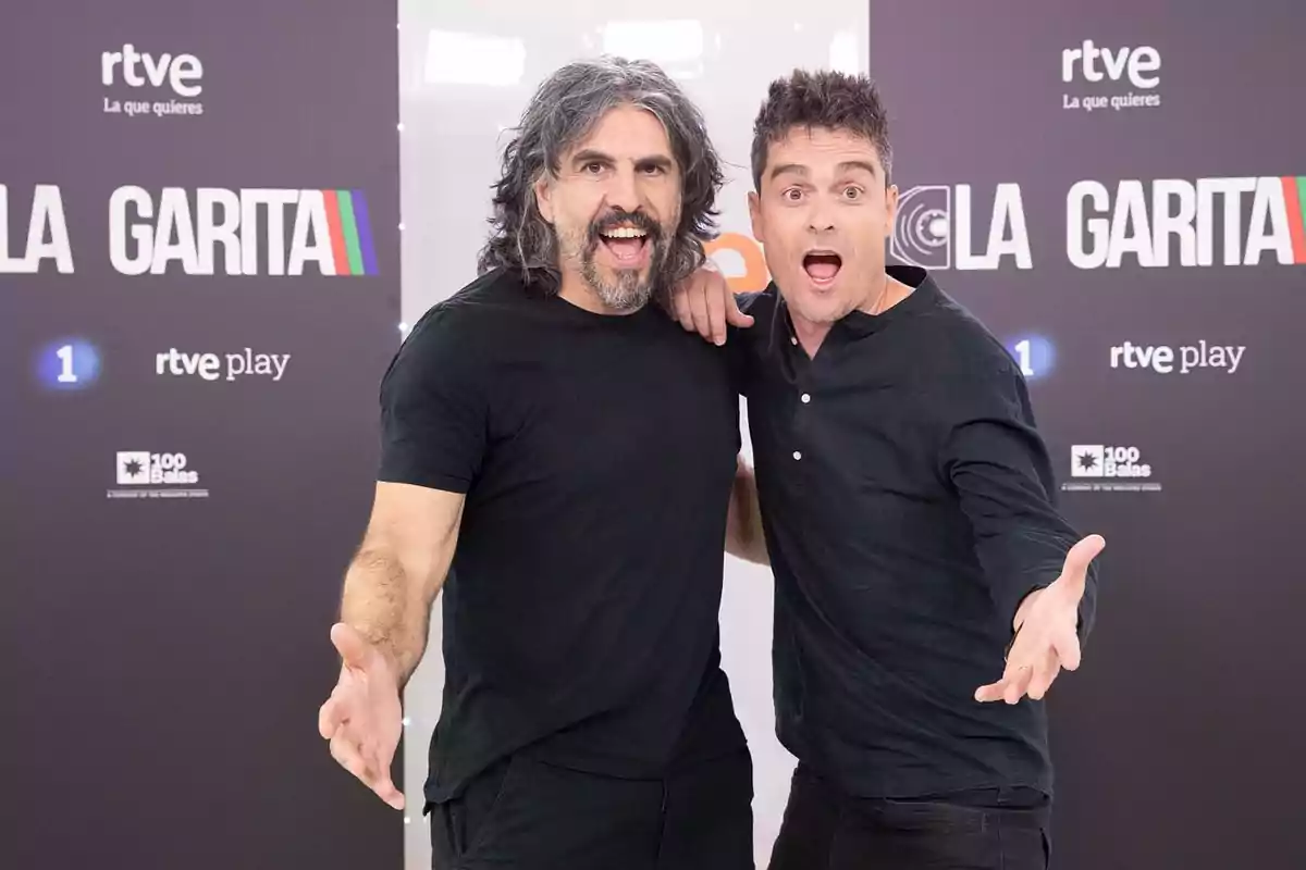 Dos hombres posan sonrientes y con gestos expresivos frente a un fondo promocional de un programa de televisión de RTVE Dos hombres posan sonrientes y con gestos expresivos frente a un fondo promocional de un programa de televisión de RTVE