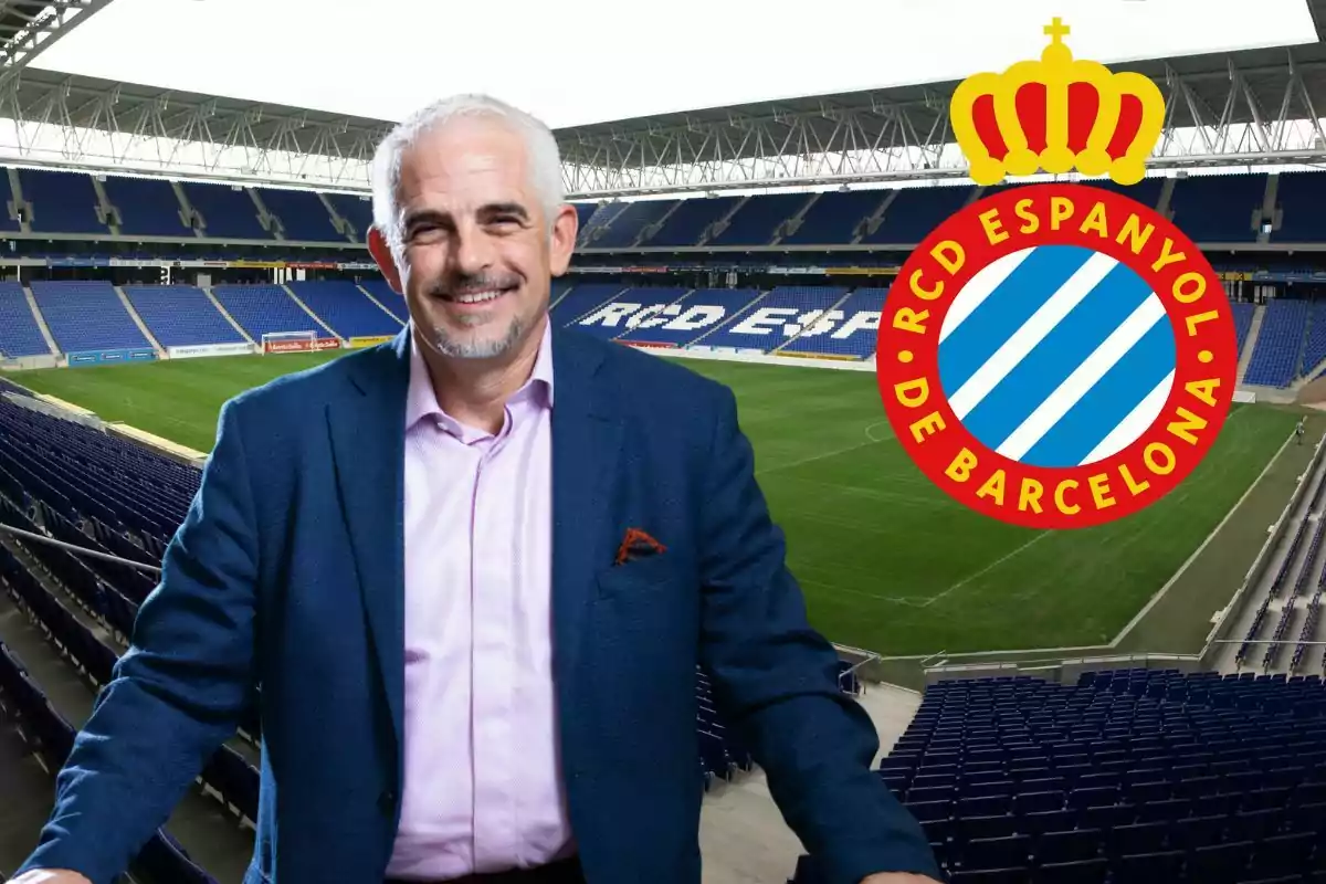 Hombre de cabello canoso y barba sonriente con saco azul y camisa rosa posando en un estadio de fútbol vacío con el escudo del RCD Espanyol de Barcelona al fondo