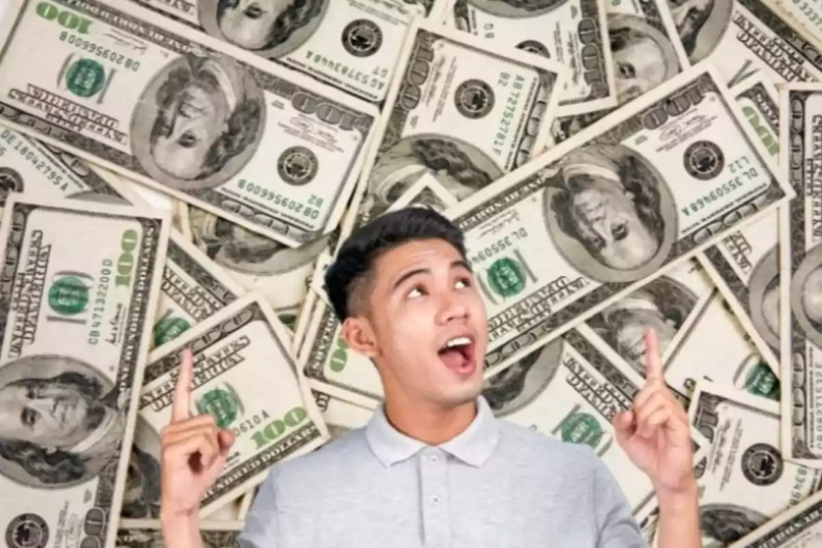 Hombre joven sonriente señalando hacia arriba con ambas manos frente a un fondo de billetes de cien dólares estadounidenses