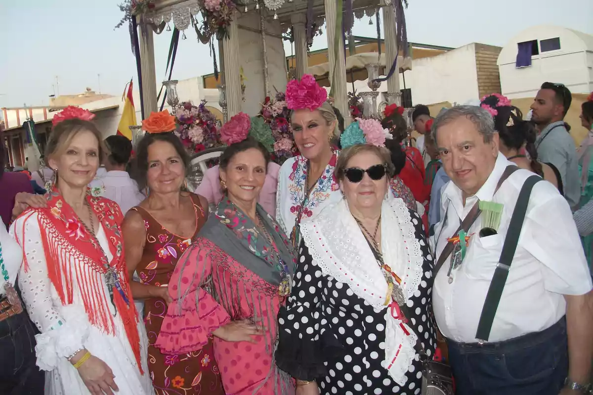 Grupo de personas vestidas con trajes típicos andaluces posando sonrientes durante una celebración popular al aire libre