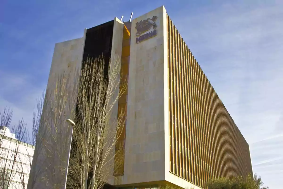 Edificio moderno de varios pisos con el logotipo de Nestlé en la parte superior y árboles sin hojas al frente Edificio moderno de varios pisos con el logotipo de Nestlé en la parte superior y árboles sin hojas al frente