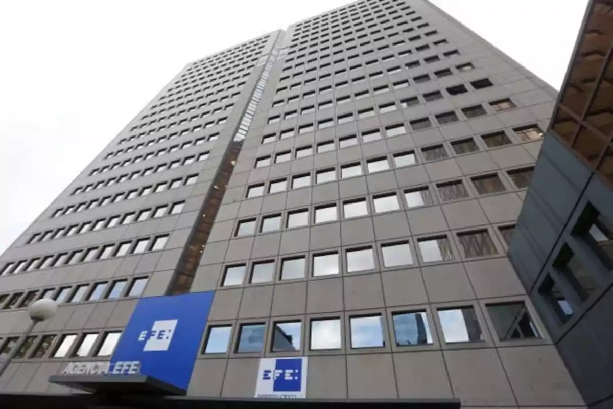 Edificio alto de oficinas con muchas ventanas y un letrero azul de la Agencia EFE en la entrada Edificio alto de oficinas con muchas ventanas y un letrero azul de la Agencia EFE en la entrada