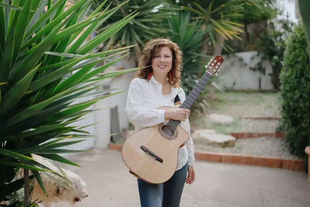 Mujer sonriente con guitarra en un jardín rodeada de plantas y un perro blanco a su lado Mujer sonriente con guitarra en un jardín rodeada de plantas y un perro blanco a su lado