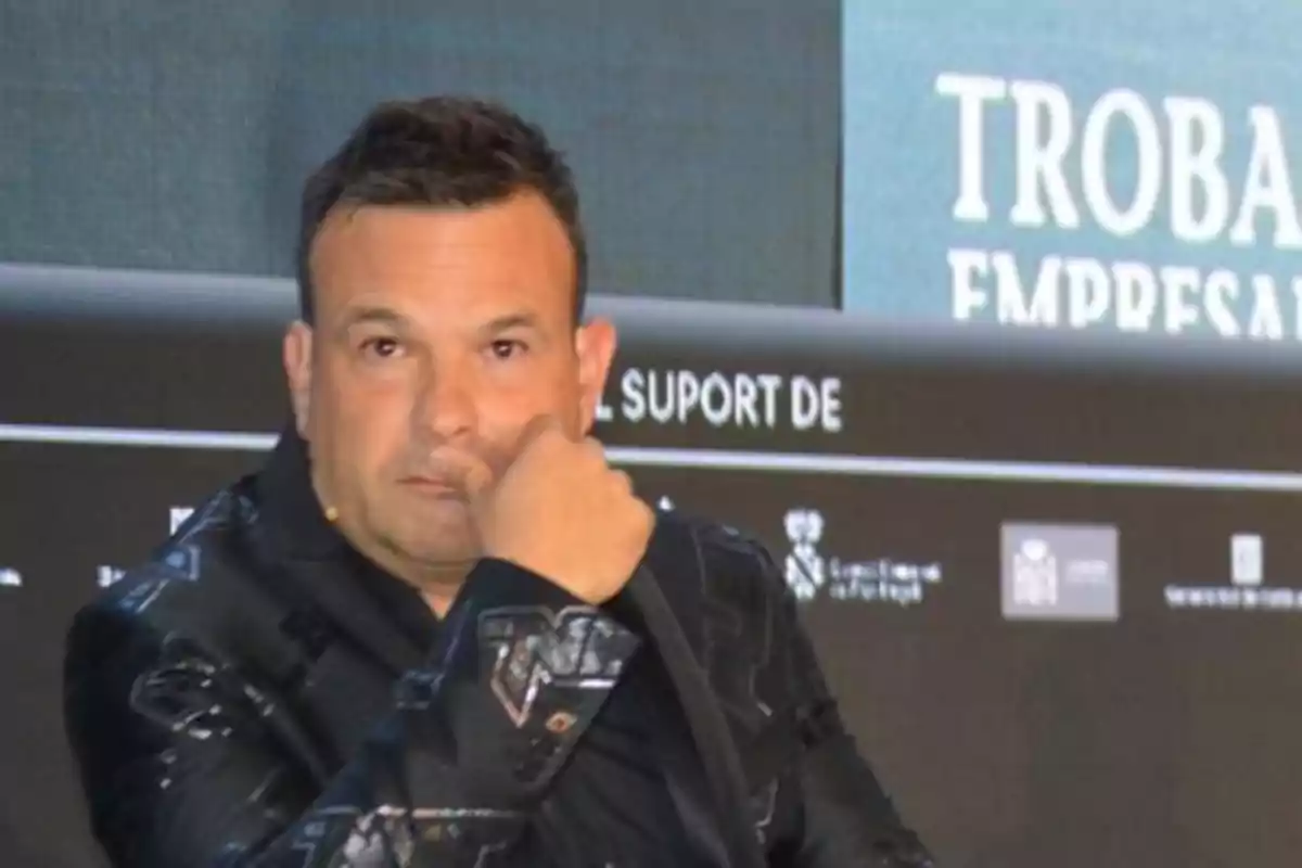 Hombre con chaqueta oscura sentado en un evento empresarial mirando al frente con expresión seria Hombre con chaqueta oscura sentado en un evento empresarial mirando al frente con expresión seria
