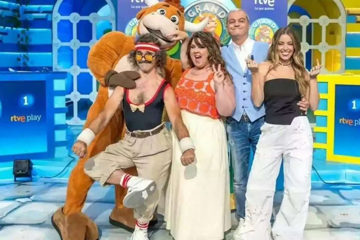 Cinco personas posan sonrientes en un set de televisión colorido, una de ellas lleva un disfraz de toro y el ambiente es alegre y divertido Cinco personas posan sonrientes en un set de televisión colorido, una de ellas lleva un disfraz de toro y el ambiente es alegre y divertido