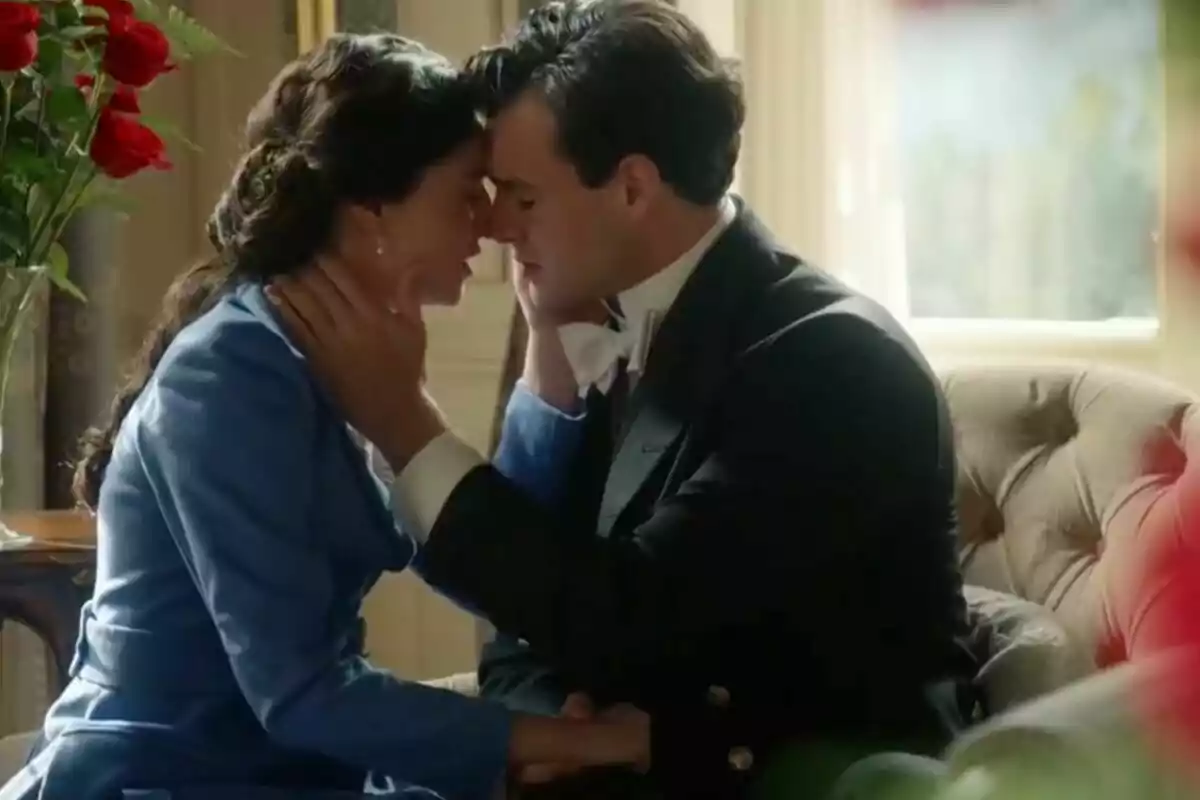 Pareja vestida de época sentada en un sofá, que son Curro y Ángela en 'La Promesa', tocándose la frente y mirándose con ternura mientras se toman de las manos. Pareja vestida de época sentada en un sofá, que son Curro y Ángela en 'La Promesa', tocándose la frente y mirándose con ternura mientras se toman de las manos.