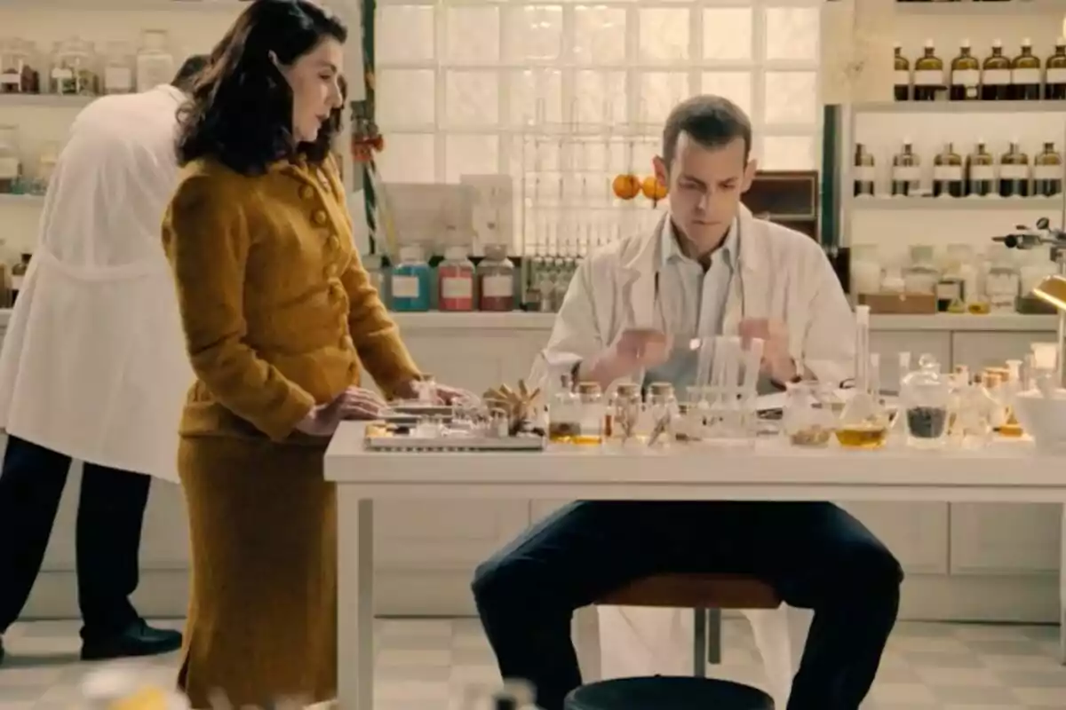 Dos personas en un laboratorio rodeados de frascos y material científico mientras una de ellas trabaja en la mesa y la otra observa en una escena de 'Sueños de Libertad'.
