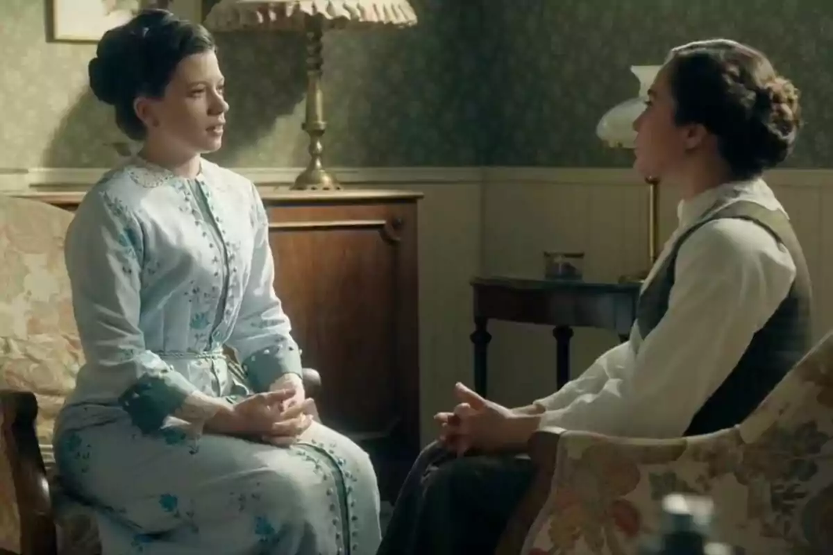 Dos mujeres con peinados recogidos y ropa de época, que son Amparo Piñero y Carmen Asecas, conversan sentadas en una sala decorada con muebles antiguos y lámparas clásicas. Dos mujeres con peinados recogidos y ropa de época, que son Amparo Piñero y Carmen Asecas, conversan sentadas en una sala decorada con muebles antiguos y lámparas clásicas.