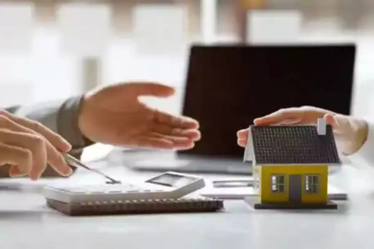 Dos personas conversan sobre la compra de una casa usando una calculadora y un modelo de vivienda sobre una mesa