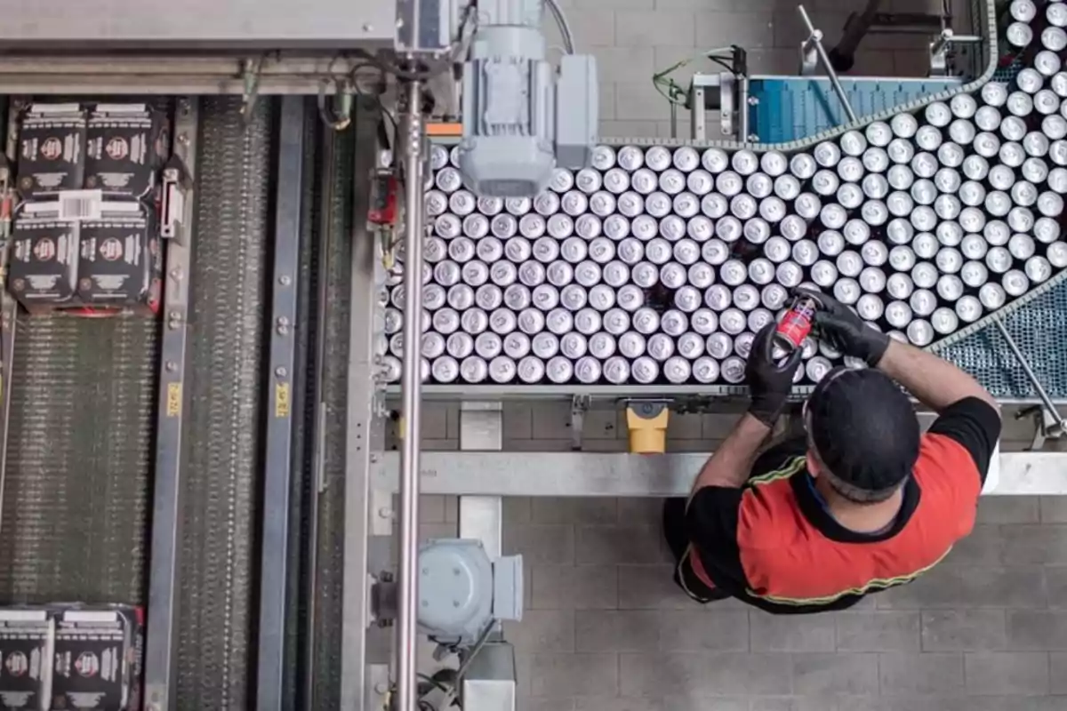 Trabajador revisando latas en una línea de producción dentro de una fábrica de bebidas Trabajador revisando latas en una línea de producción dentro de una fábrica de bebidas