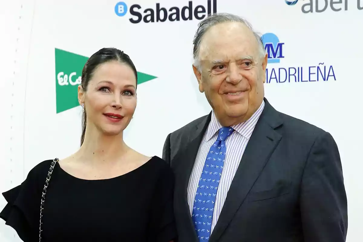 Una mujer y un hombre posan juntos en un evento formal con fondo de logotipos de marcas.
