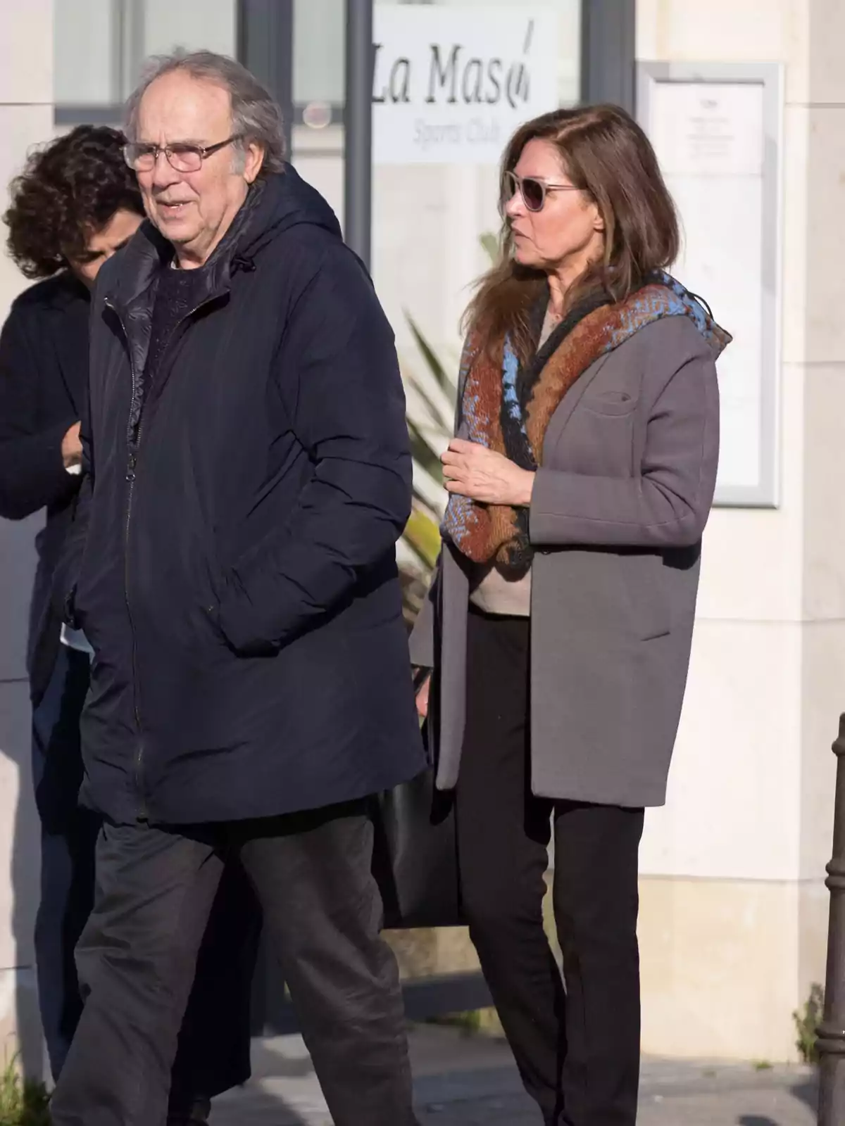 Dos personas adultas caminan por la calle abrigadas con ropa de invierno mientras conversan bajo la luz del sol. Dos personas adultas caminan por la calle abrigadas con ropa de invierno mientras conversan bajo la luz del sol.