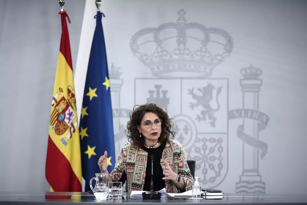 Mujer hablando en una rueda de prensa con las banderas de España y la Unión Europea detrás Mujer hablando en una rueda de prensa con las banderas de España y la Unión Europea detrás