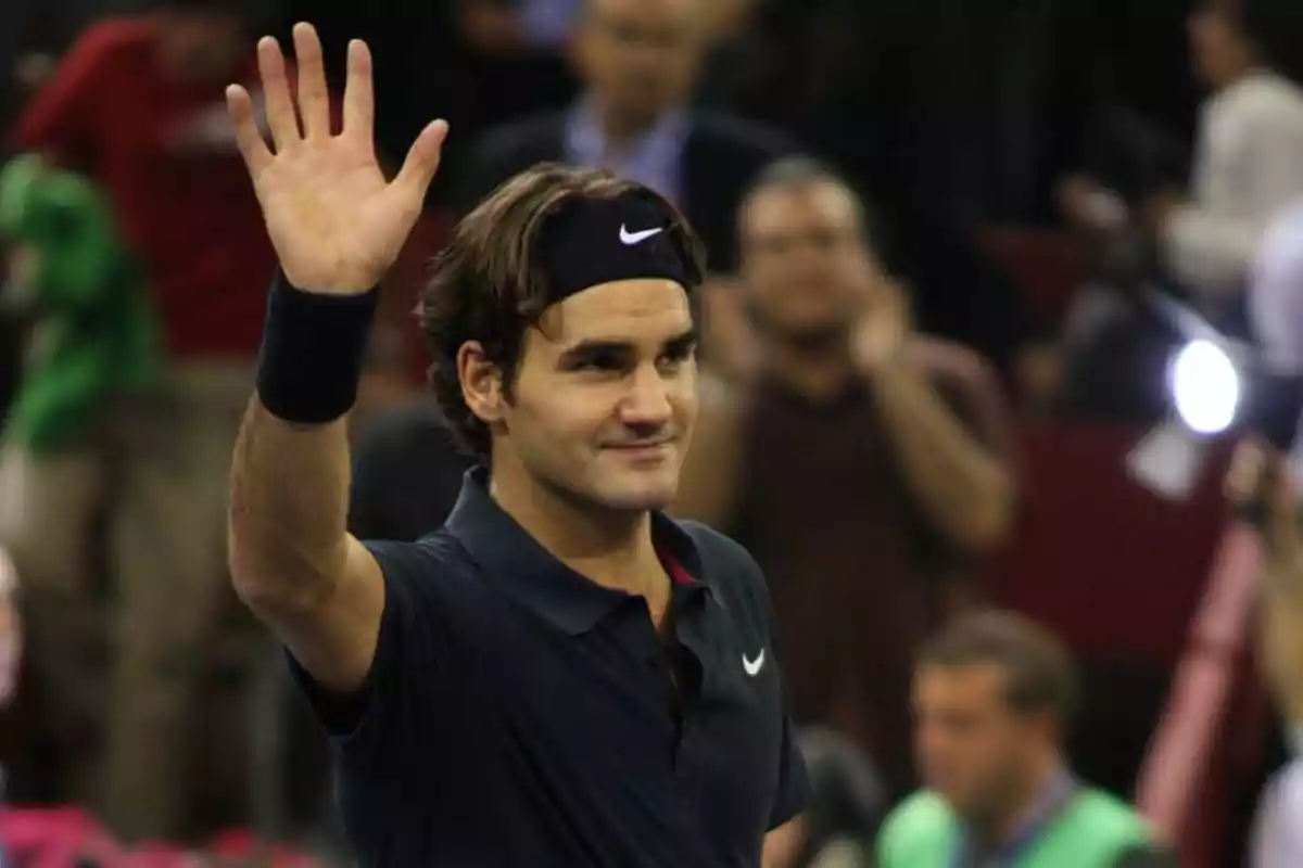 Tennis player waving to the crowd with a raised hand on an indoor court