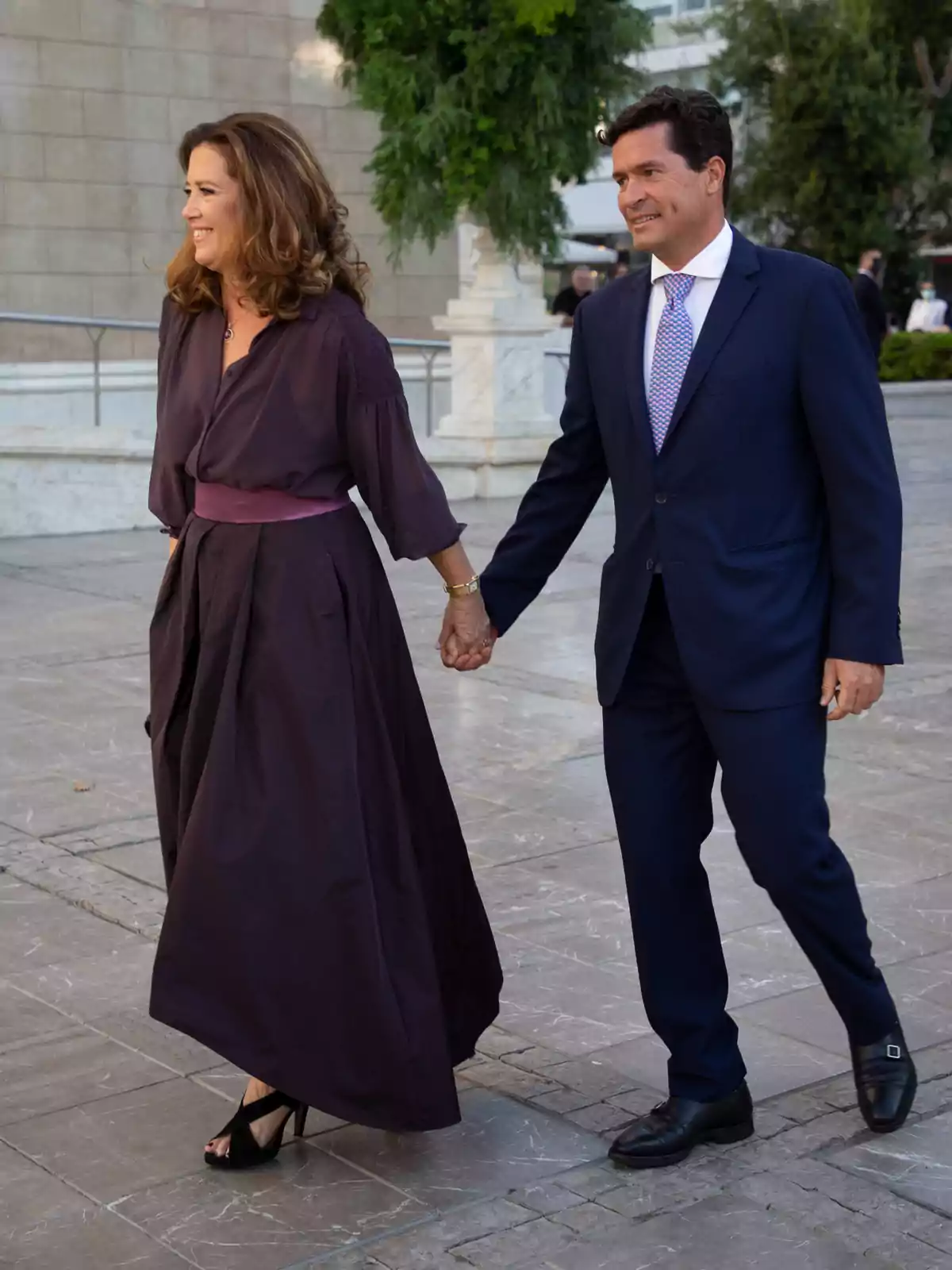 Pareja elegantemente vestida caminando de la mano en un espacio al aire libre Pareja elegantemente vestida caminando de la mano en un espacio al aire libre
