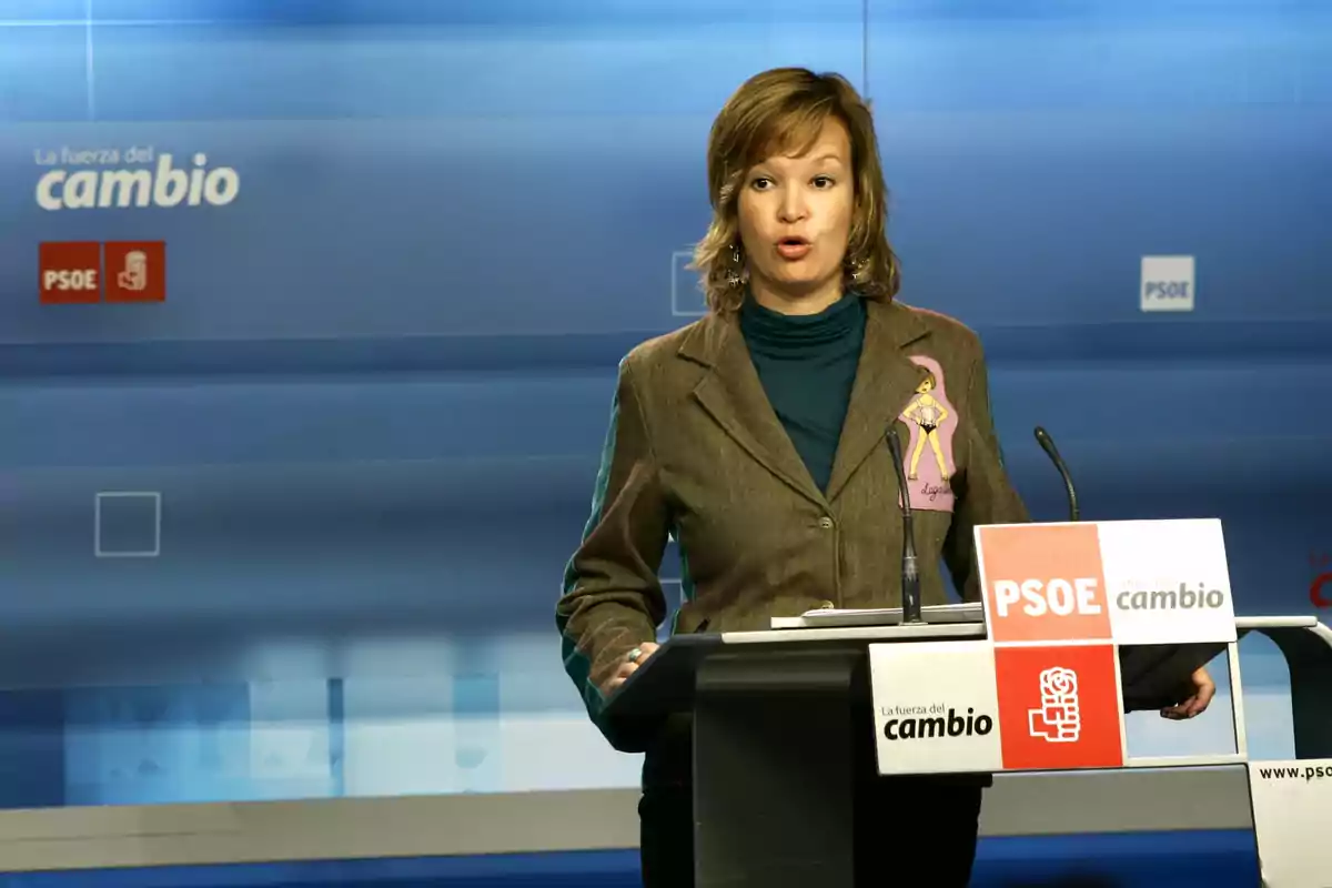 Mujer hablando en un atril con logotipos del PSOE y el lema La fuerza del cambio en el fondo Mujer hablando en un atril con logotipos del PSOE y el lema La fuerza del cambio en el fondo