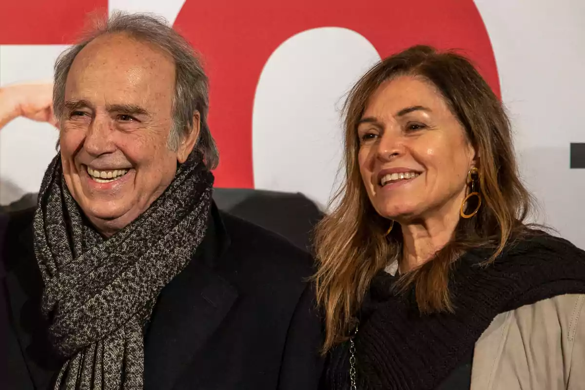 Una pareja sonriente posa frente a un fondo blanco y rojo en un evento