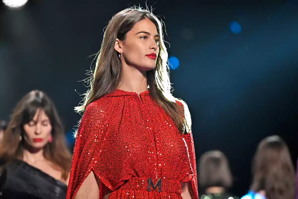 Modelo desfilando en una pasarela con un vestido rojo brillante y fondo oscuro con luces desenfocadas Modelo desfilando en una pasarela con un vestido rojo brillante y fondo oscuro con luces desenfocadas