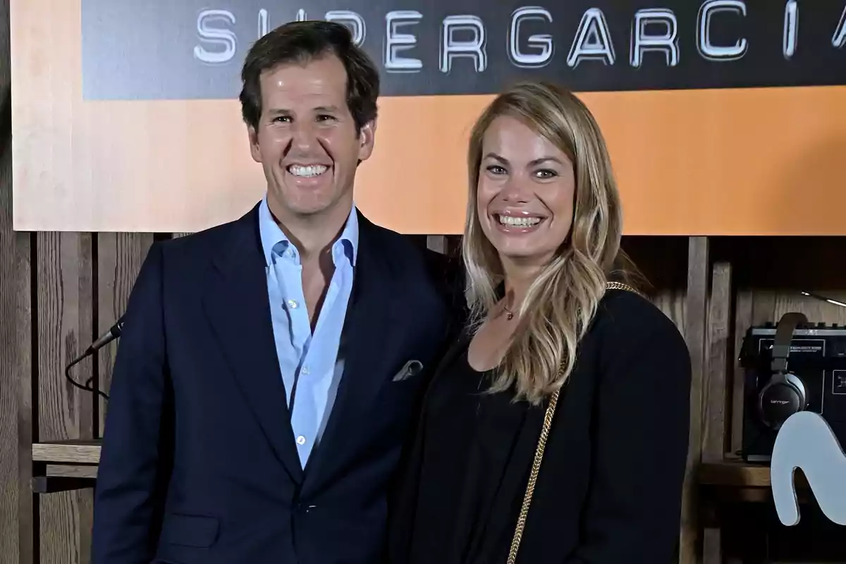 Una pareja sonriente posa frente a un cartel en un evento elegante